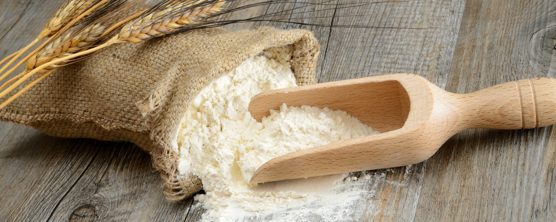 Wooden table with a sack of flour and spoon with ears