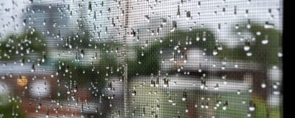 Window screen in front of a window with raindrops on it