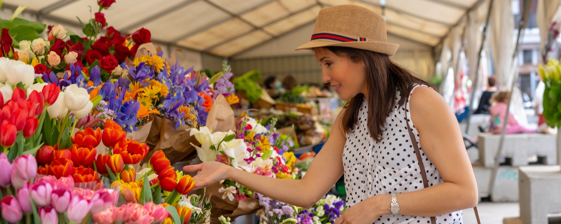 A pretty tourist with a photo camera visiting a flower market, enjoying spring.