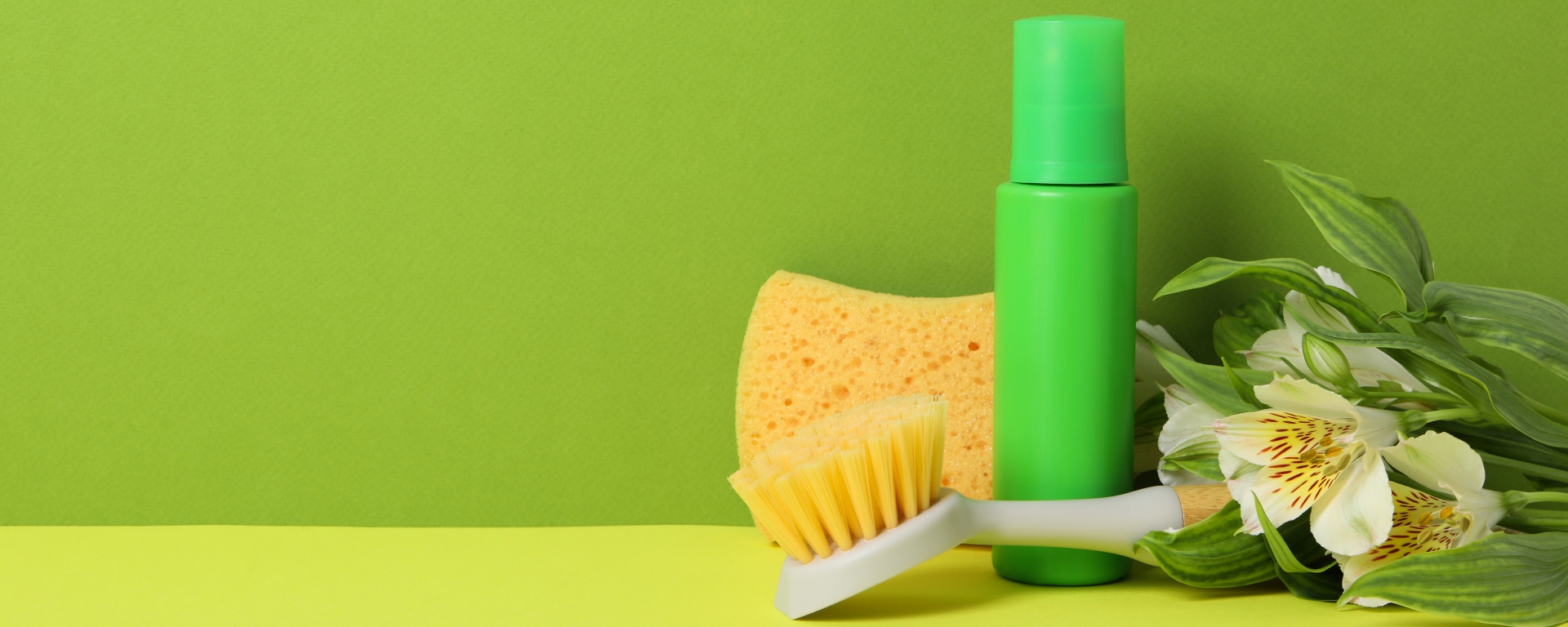 Flowers and cleaning tools in front of a green background. Spring cleaning concept.